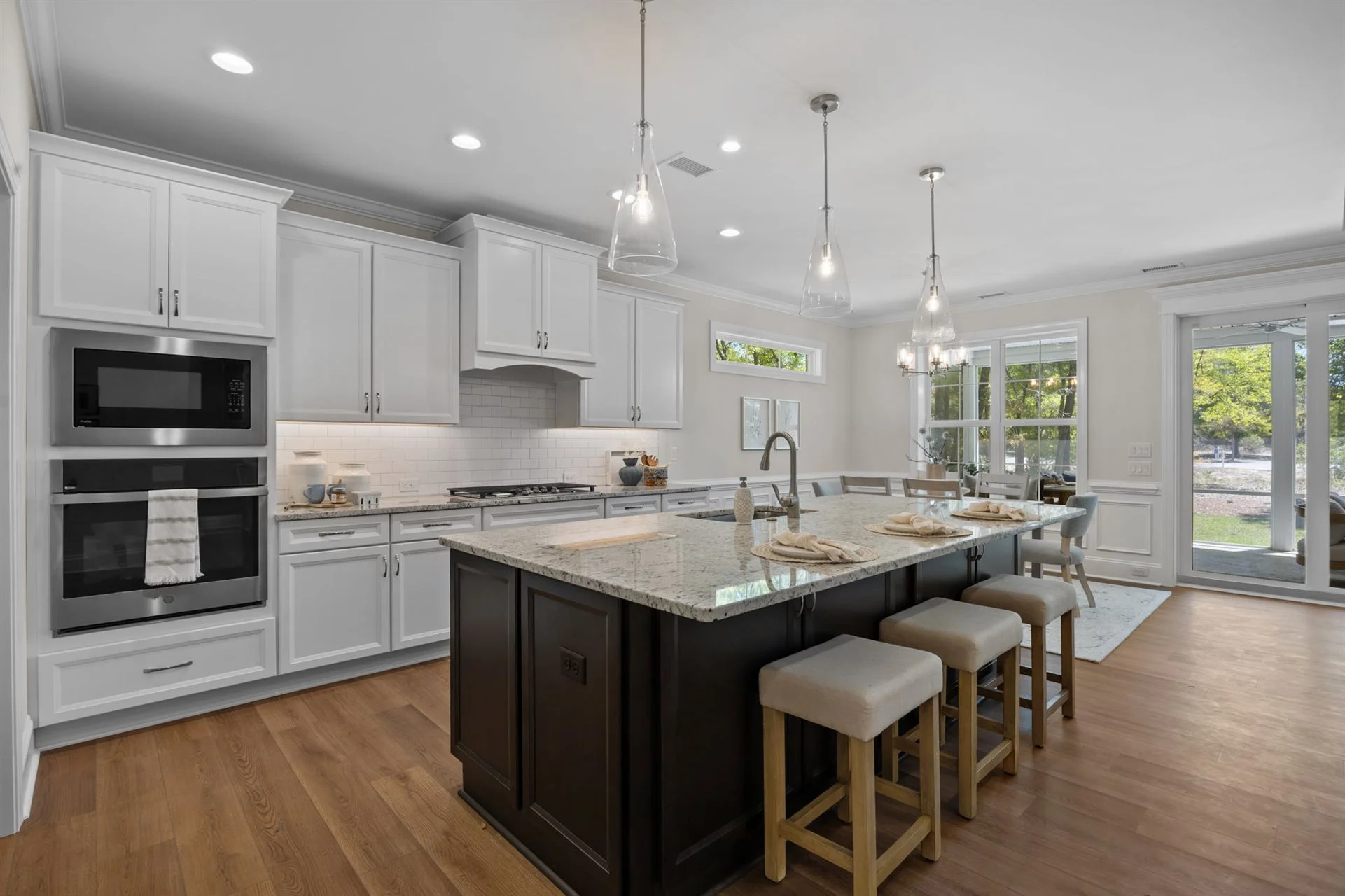 Spacious kitchen with large island, granite countertops, white cabinets, hardwood floor, and modern lighting. Ideal for a home builder showcase.