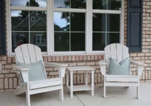 Two white Adirondack chairs with cushions and a small table on a brick porch, showcasing home builder design and craftsmanship.