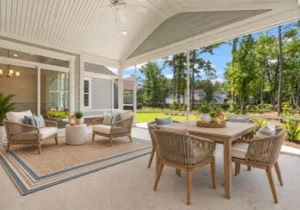 Spacious patio with outdoor seating, wooden dining set, and ceiling fan, overlooking a lush backyard. Ideal design inspiration for home builders.